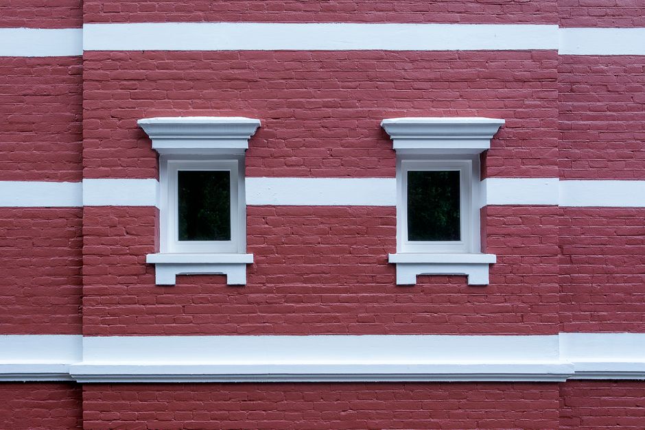 Deux fenêtres à cadre blanc encastrées dans une façade de brique rouge, vue depuis l'extérieur.