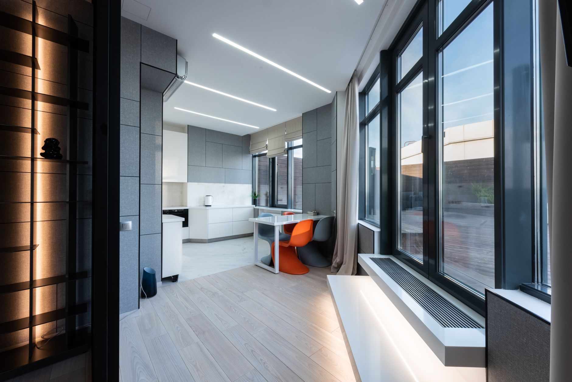 Intérieur moderne et lumineux avec de grandes fenêtres à cadre foncé donnant sur un séjour au parquet clair.